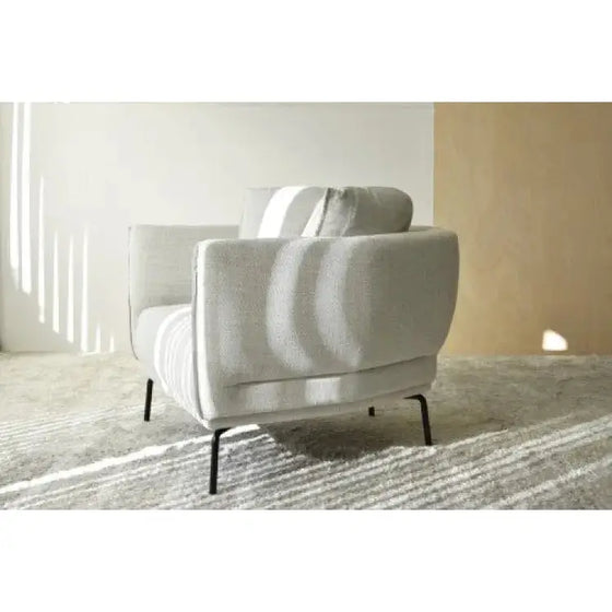 Una silla Sillón Tapizada en Mezclilla Beige sentada sobre una alfombra en una habitación.