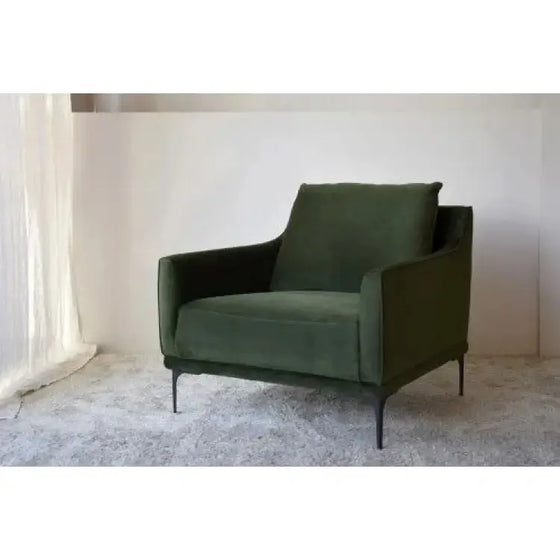 A Sillón Terciopelo Verde - Terciopelo y Metal frente a una pared blanca.