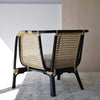 El Sillón Vintage en Ratán Julia, con marco negro y respaldo y laterales de caña tejida, reposa elegantemente sobre una alfombra texturizada, mostrando la decoración contemporánea.
