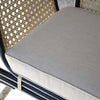 Un primer plano del Sillón Vintage en Ratán Julia muestra un asiento acolchado de color beige, o cojín crema, con un respaldo de ratán tejido sobre un elegante marco de metal negro.