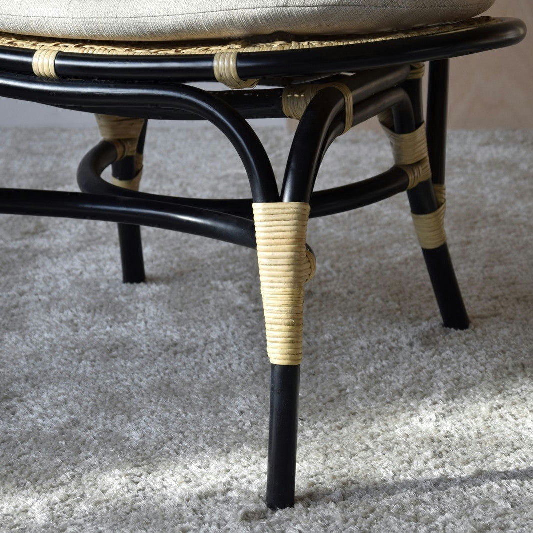 Primer plano de la pata de una silla Sillón Vintage en Ratán Norma sobre una alfombra gris texturizada, resaltando la elegancia de su diseño exclusivo.
