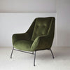 El Sillón de Diseño en Terciopelo Verde "Oscuro" cuenta con un respaldo capitoné y se apoya elegantemente sobre patas de metal negro, elevando su decoración e interiorismo sobre un piso alfombrado claro.