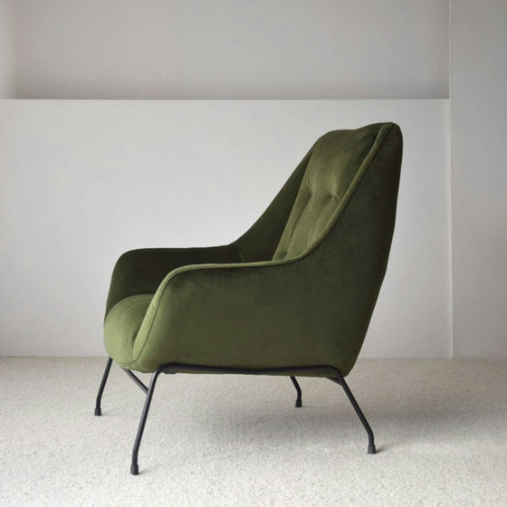 El Sillón de Diseño en Terciopelo Verde "Oscuro" ofrece una elegante combinación de confort y confort, destacando su moderno estilo con patas de metal negro sobre una alfombra clara.