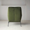 Un Sillón de Diseño en Terciopelo Verde "Oscuro" con estilo moderno y patas de metal negro, elegantemente colocado sobre un piso alfombrado claro en una habitación minimalista.