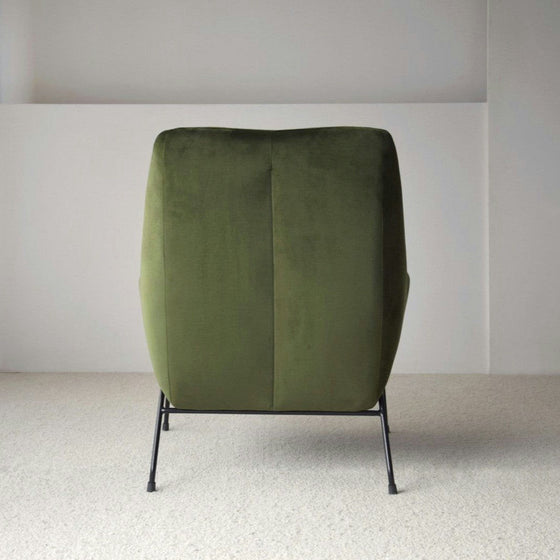 Un Sillón de Diseño en Terciopelo Verde "Oscuro" con estilo moderno y patas de metal negro, elegantemente colocado sobre un piso alfombrado claro en una habitación minimalista.