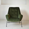 El sillón de diseño de terciopelo verde "Oscuro" con patas de metal negro reposa elegantemente sobre un suelo de moqueta clara, encarnando un estilo interior moderno.