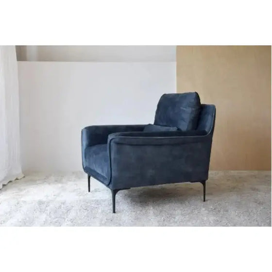 Un Sillón de Terciopelo Azul Desgastado - Elegancia Urbana frente a una pared blanca rezuma elegancia y encanto urbano contemporáneo. El terciopelo azul desgastado añade un toque de encanto vintage al espacio.