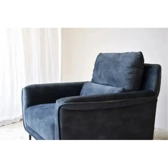 Un Sillón de Terciopelo Azul Desgastado - Elegancia Urbana colocado elegantemente frente a una ventana rezuma Elegancia Urbana.