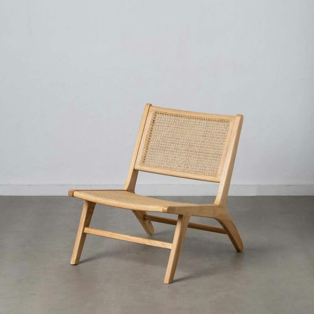 El Sillón en Madera y Ratán Sven, con un asiento y respaldo de ratán tejido, frente a una pared azul claro y un piso gris, encarna el diseño contemporáneo.
