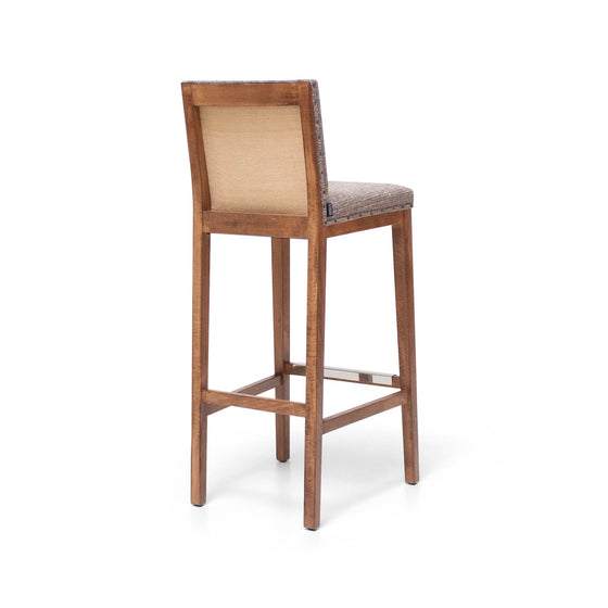 El Taburete Alto en Madera y Tapizado Max Vintage, con respaldo y asiento acolchados en color beige, irradia elegancia retro cuando se ve desde atrás sobre un fondo blanco. Este taburete de bar está elaborado con Madera de Haya Maciza, lo que garantiza durabilidad y estilo.