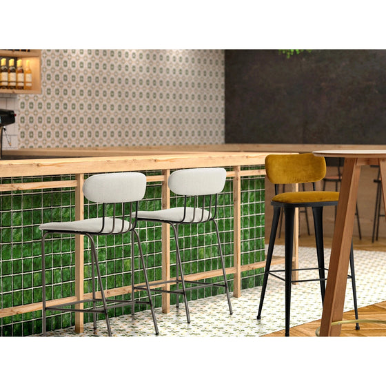 Un área de bar moderna con dos taburetes acolchados grises y un taburete acolchado amarillo en un mostrador de madera, con respaldo y asiento tapizados para mayor comodidad. El Taburete Alto en Metal y Tapìzado Miki cuenta con un diseño ergonómico, mientras que la malla de alambre y la vegetación debajo complementan el fondo de mosaico estampado.