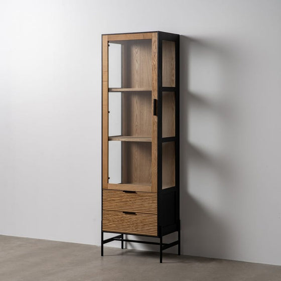 VITRINA NEGRO-NATURAL DM-MADERA 61 X 40 X 196 CM, un gabinete alto y estrecho de madera con frente de vidrio con detalles de metal negro y una puerta elegante, que presenta cuatro estantes abiertos y dos cajones en la parte inferior, apoyado contra una pared blanca lisa sobre un piso de concreto.