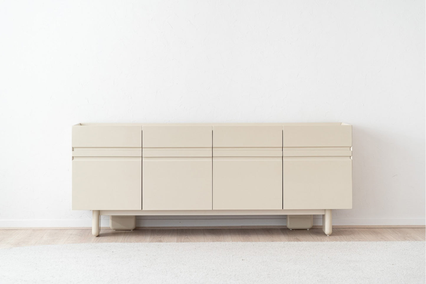 Un aparador de DM lacado beige brillo con sobre cerámico (200×48×80 cm) destaca junto a una pared blanca sobre suelo de madera clara y alfombra suave, ideal como mueble comedor moderno o para almacenaje en el salón.