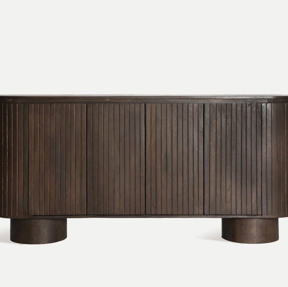 El aparador Kolga de inspiración Art Decó, hecho de madera de mango oscuro, presenta puertas con listones verticales y se apoya elegantemente sobre dos patas cilíndricas.
