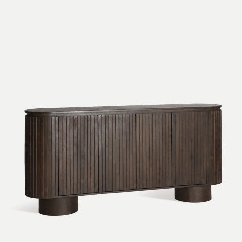 El aparador Kolga, de inspiración Art Decó, está elaborado en madera de mango oscura, presenta ranuras verticales, bordes redondeados y dos patas cilíndricas.