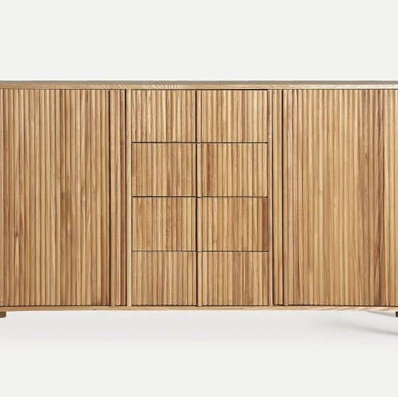 Explora el Aparador de madera DM y paulownia (160x40x90 cm) Skagen, un aparador de madera con ranuras verticales y un diseño moderno. Fabricado con madera de paulownia de primera calidad, incluye dos armarios y cuatro cajones centrales, combinando a la perfección elegancia y funcionalidad.