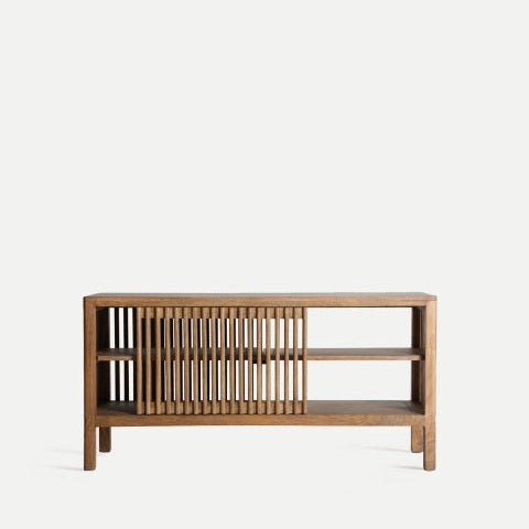 Aparador de madera de mango (121x36x61 cm) Trevoux es un aparador de estilo nórdico minimalista que presenta estantes abiertos a la derecha y listones verticales a la izquierda, elaborados con madera de mango de primera calidad sobre un fondo liso para un toque elegante.