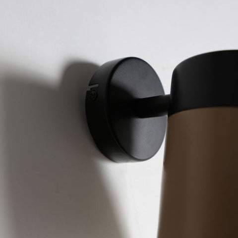 Un primer plano del Aplique de pared en hierro negro y dorado Aston, una lámpara de pared de estilo art decó, elegantemente colocada sobre una pared blanca.