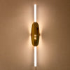 La Lámpara de Pared Xago Elegante y Moderna es una luminaria vertical con un diseño elegante, que presenta una pieza central dorada alargada entre barras blancas iluminadas que utilizan iluminación LED para crear un cálido brillo en la pared.