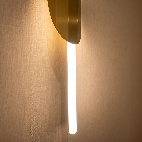 La Lámpara de Pared Xago Elegante y Moderna ofrece un diseño contemporáneo con una luminaria cilíndrica vertical que emite un brillo suave en la pared beige gracias a su iluminación LED.