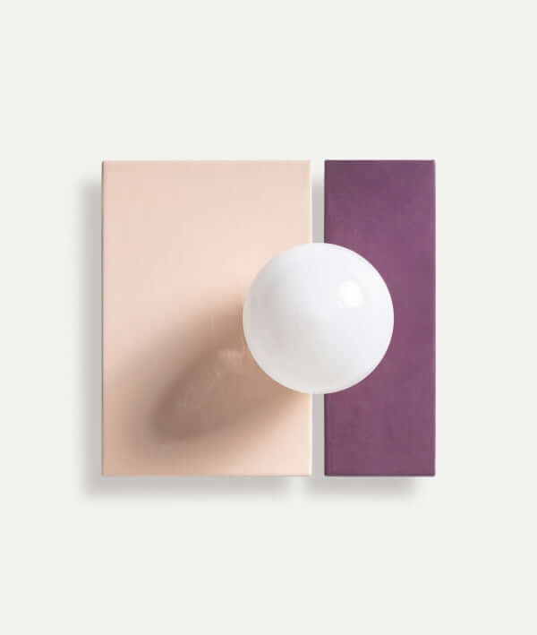 Una bombilla redonda blanca está montada sobre el aplique de pared de hierro oro y vidrio morado URU 30×19×31 cm, que presenta un diseño minimalista con detalles de hierro dorado y vidrio morado sobre un fondo liso.