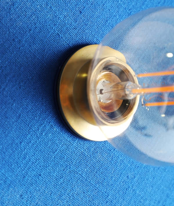 Un primer plano del aplique contemporáneo VETRA de algodón azul y metal dorado (33×9×33 cm) montado sobre una superficie azul texturizada, perfecto para iluminación decorativa.