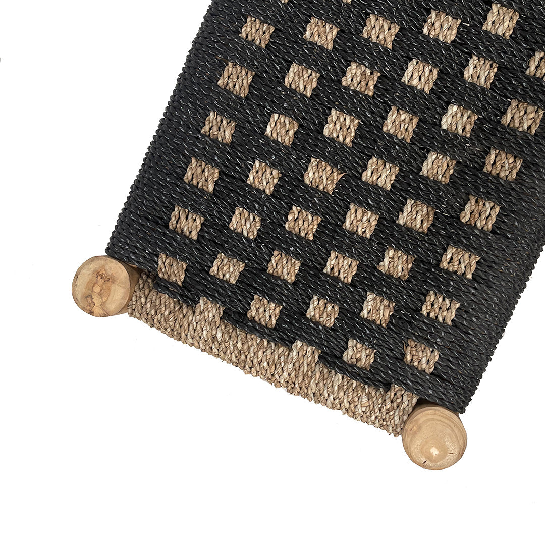Primer plano de un tapete tejido con patrón de cuadros negros y naturales, fijado por dos clavijas redondas de teca, ideal como accesorio para su Banqueta de Madera de Teca y Ratán Negro/Nat.