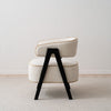 Vista lateral de un elegante y moderno Sillón tapizado en beige y madera de fresno negro Capri sobre un suelo de moqueta clara.