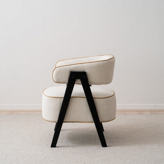 Vista lateral de un elegante y moderno Sillón tapizado en beige y madera de fresno negro Capri sobre un suelo de moqueta clara.