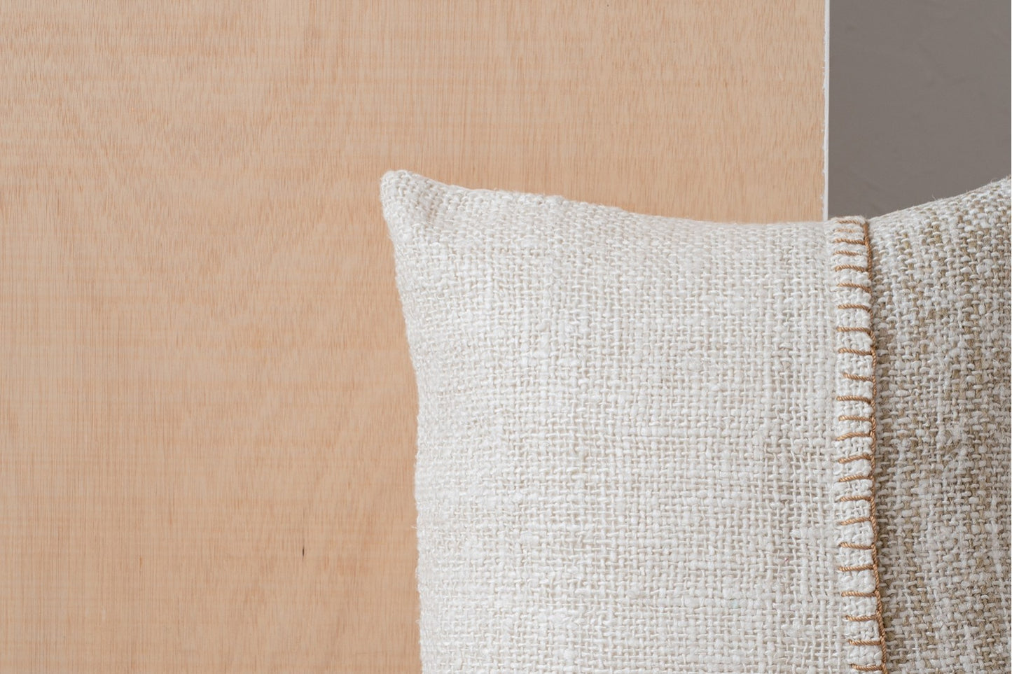 Primer plano del Cojín de algodón blanco y camel con detalle bordado 50X50CM - natural - ERO N4, mostrando su superficie texturizada y sus costuras, sobre un fondo de madera clara y una pared gris.