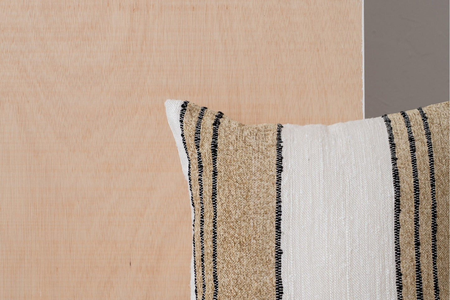 Primer plano del Cojín de algodón blanco, camel con franjas negras 50x50cm - natural - ERO N1 colocado contra una superficie de madera clara y una pared gris.