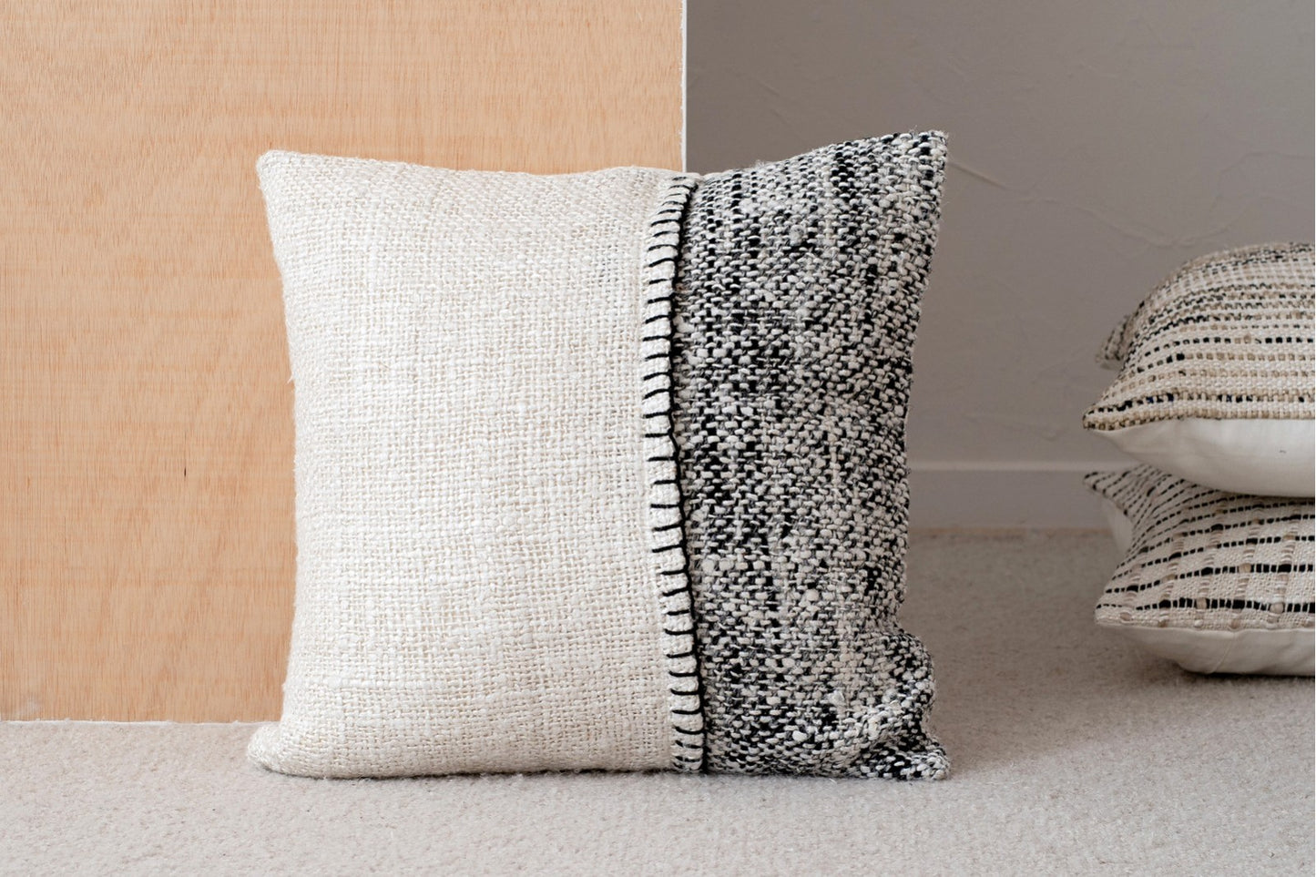 El Cojín de algodón blanco y negro con detalle bordado 50X50CM - natural - OTO N3, con tejido crema por un lado y un motivo moteado en blanco y negro por el otro, se asienta con elegancia sobre un suelo de moqueta clara.