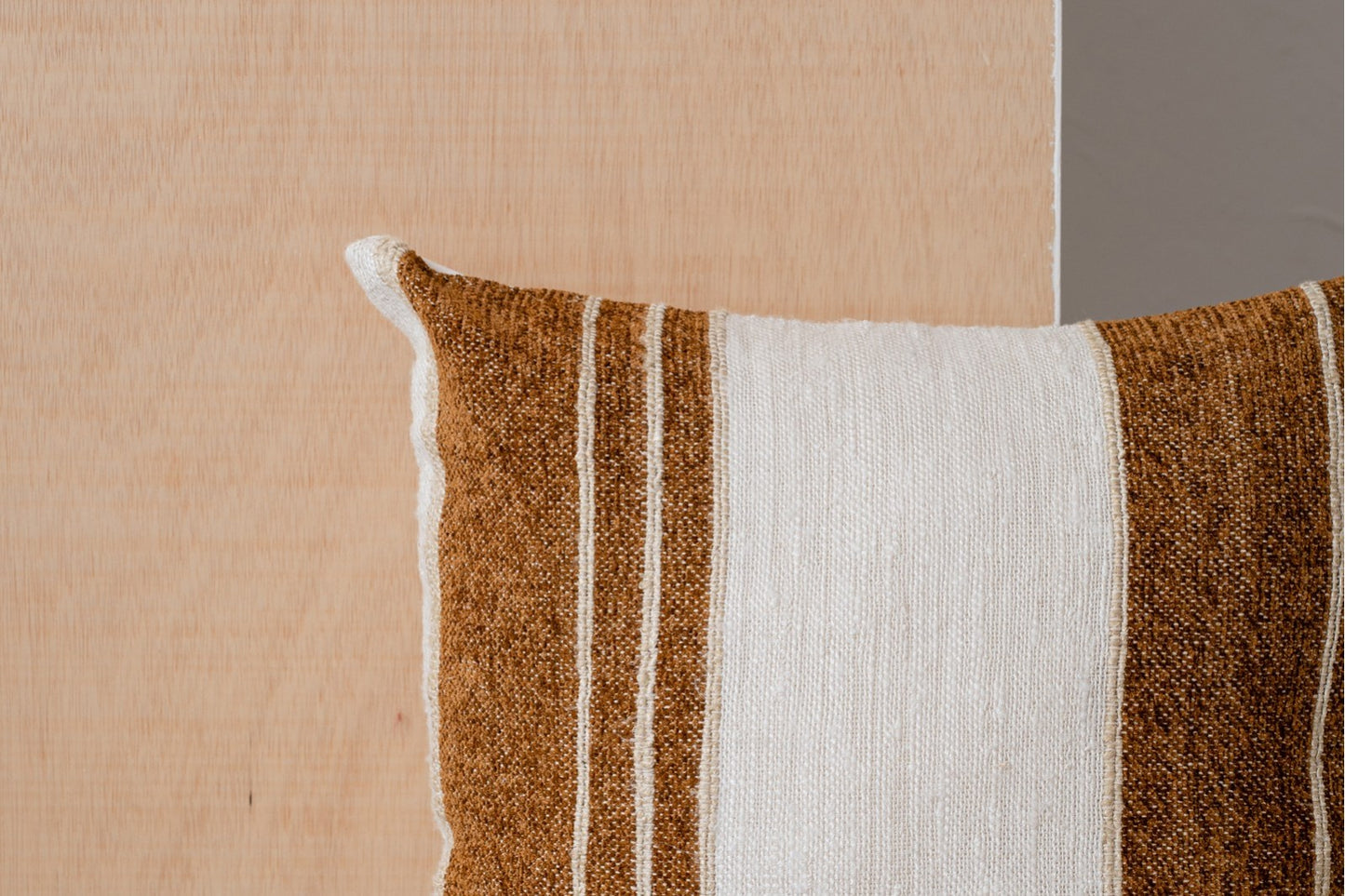 Primer plano del cojín de algodón blanco, beige y ocre con franjas 50x50CM MINIA N3, de algodón 100%, delante de una superficie de madera clara.