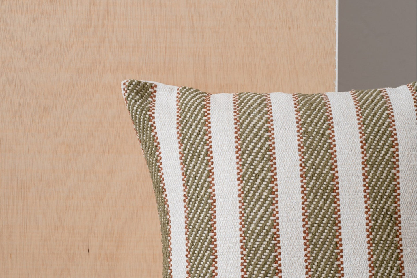 Detalle del Cojín de algodón blanco y verde oliva con franjas - natural - BERTE N1, con rayas verticales verdes y blancas, sobre un fondo de madera clara.