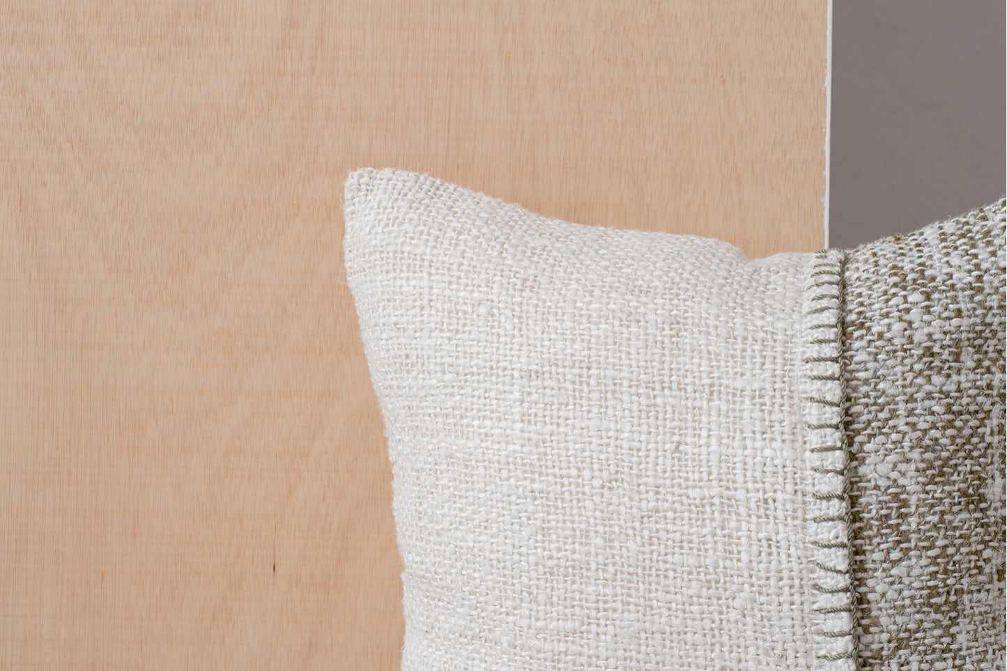 Detalle de un cojín BERTE N3, 50x50 cm, de algodón blanco y verde oliva con detalles bordados, sobre un fondo de madera clara.