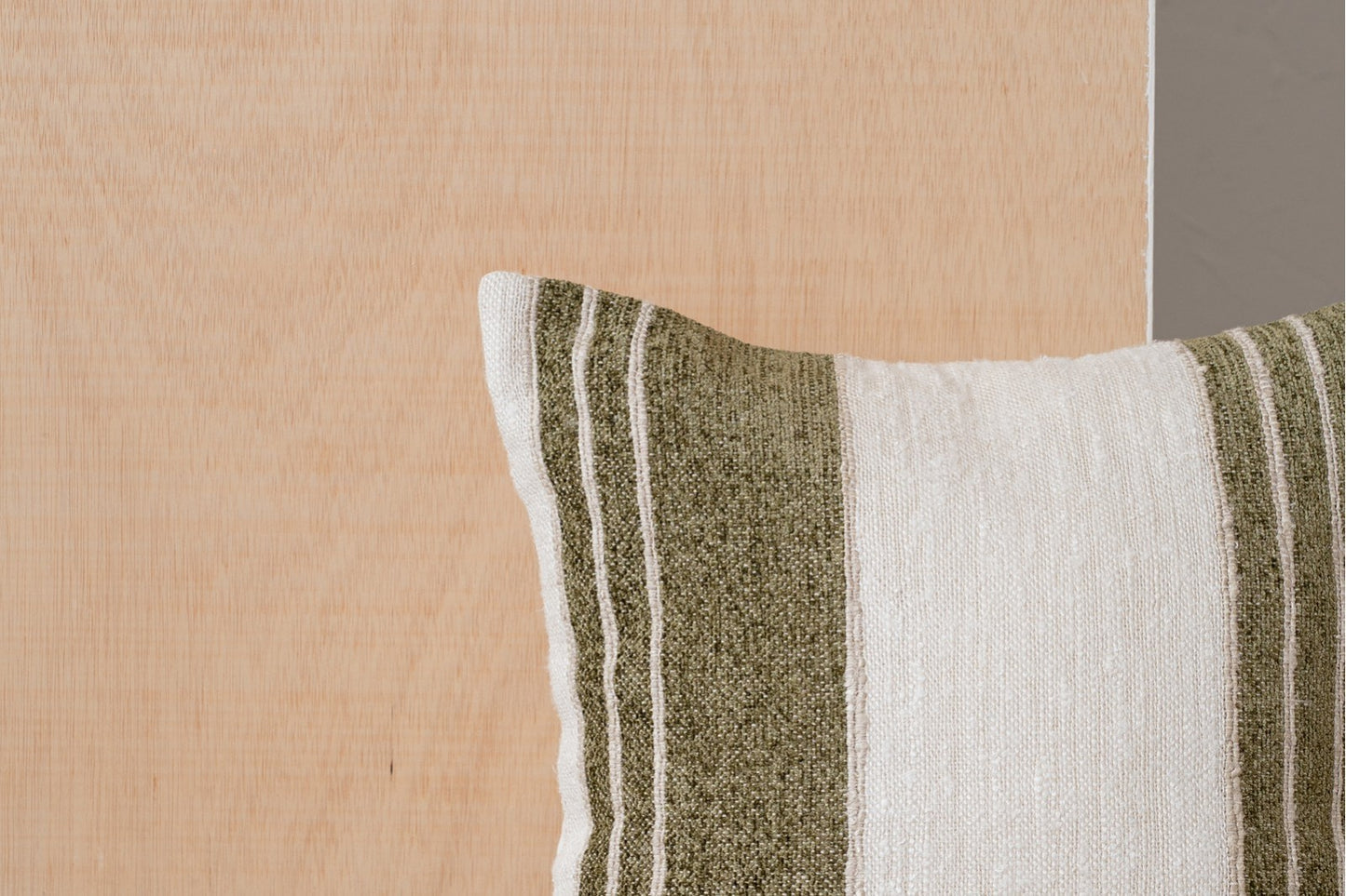 A BERTE N6 cojín de algodón blanco, beige y verde oliva con franjas (50x50cm) reposa sobre un fondo de madera clara.