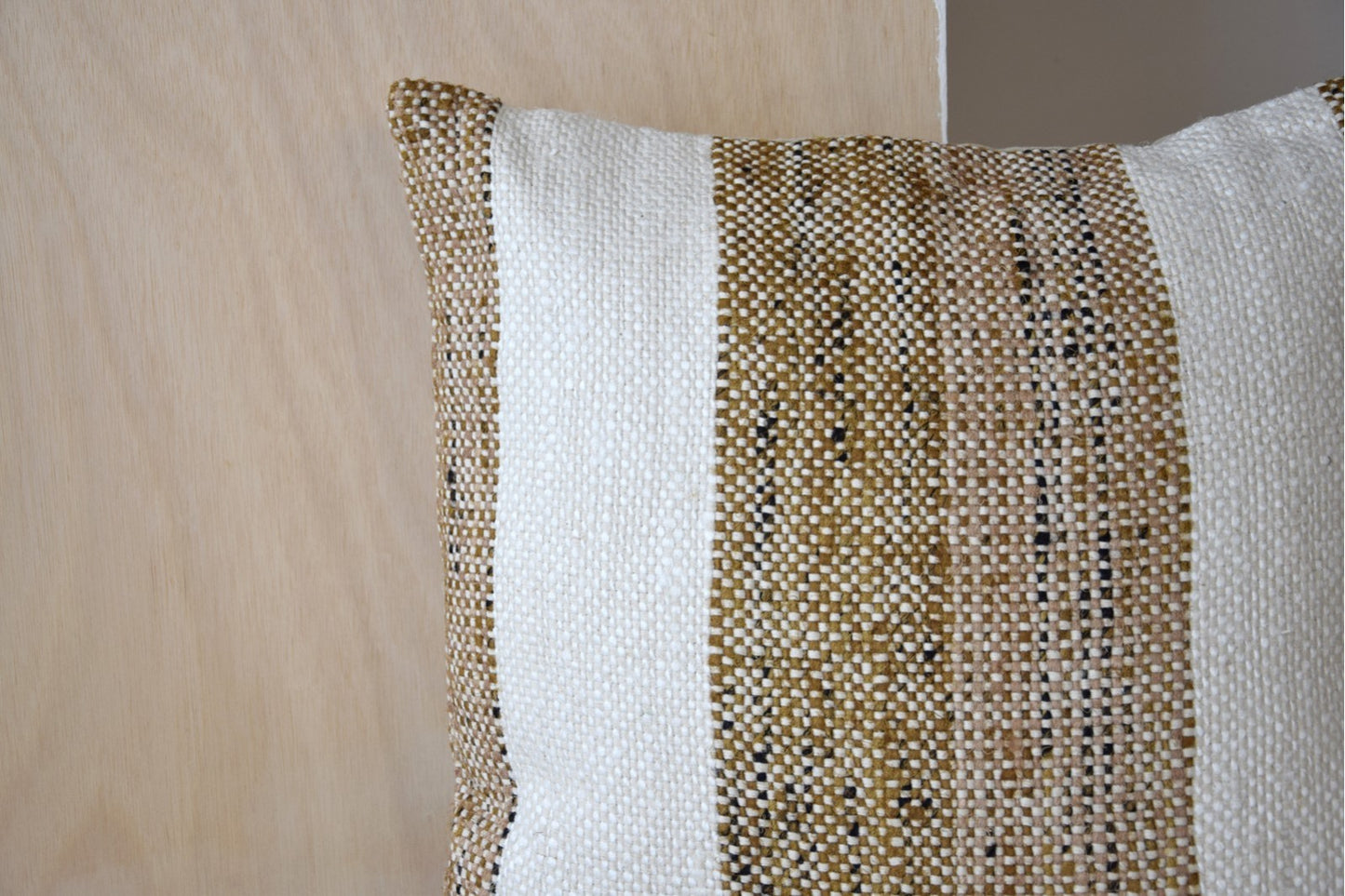Detalle del cojín de algodón mostaza y blanco con franjas 50x50cm LAZA N2, con rayas mostaza y blancas como toque decorativo sobre un fondo de madera clara y gris.