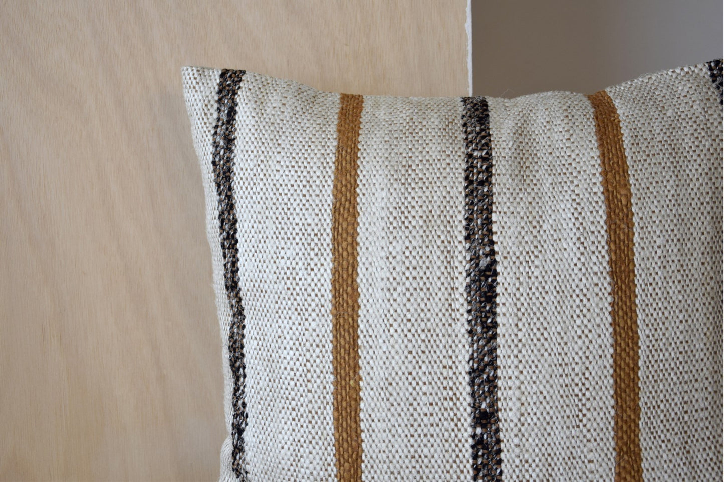 Primer plano del Cojín de algodón mostaza y blanco con líneas estrechas 50x50CM - natural - LAZA N6, que muestra su diseño de rayas estrechas, sobre un fondo de madera clara.