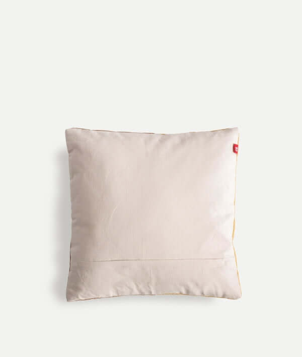 Cojín geométrico cuadrado de algodón AMAIA beige claro y ocre (45×45 cm) con una sutil costura y una pequeña etiqueta roja en la parte superior derecha, sobre un fondo blanco liso.