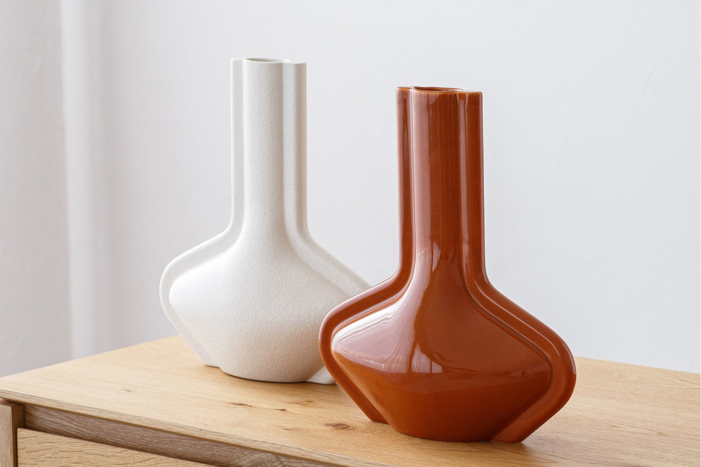 El set de jarrones de cerámica blanco mate y terracota brillo DARA, de diseño geométrico, destaca sobre una superficie clara y fondo blanco, ideal para decoración del hogar y ambientes contemporáneos.