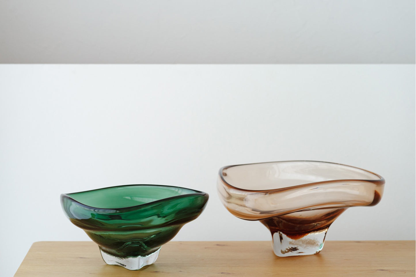 El conjunto de centros de mesa de vidrio verde y ahumado EREA, con formas orgánicas, decora cualquier espacio moderno sobre superficies de madera y fondo blanco.