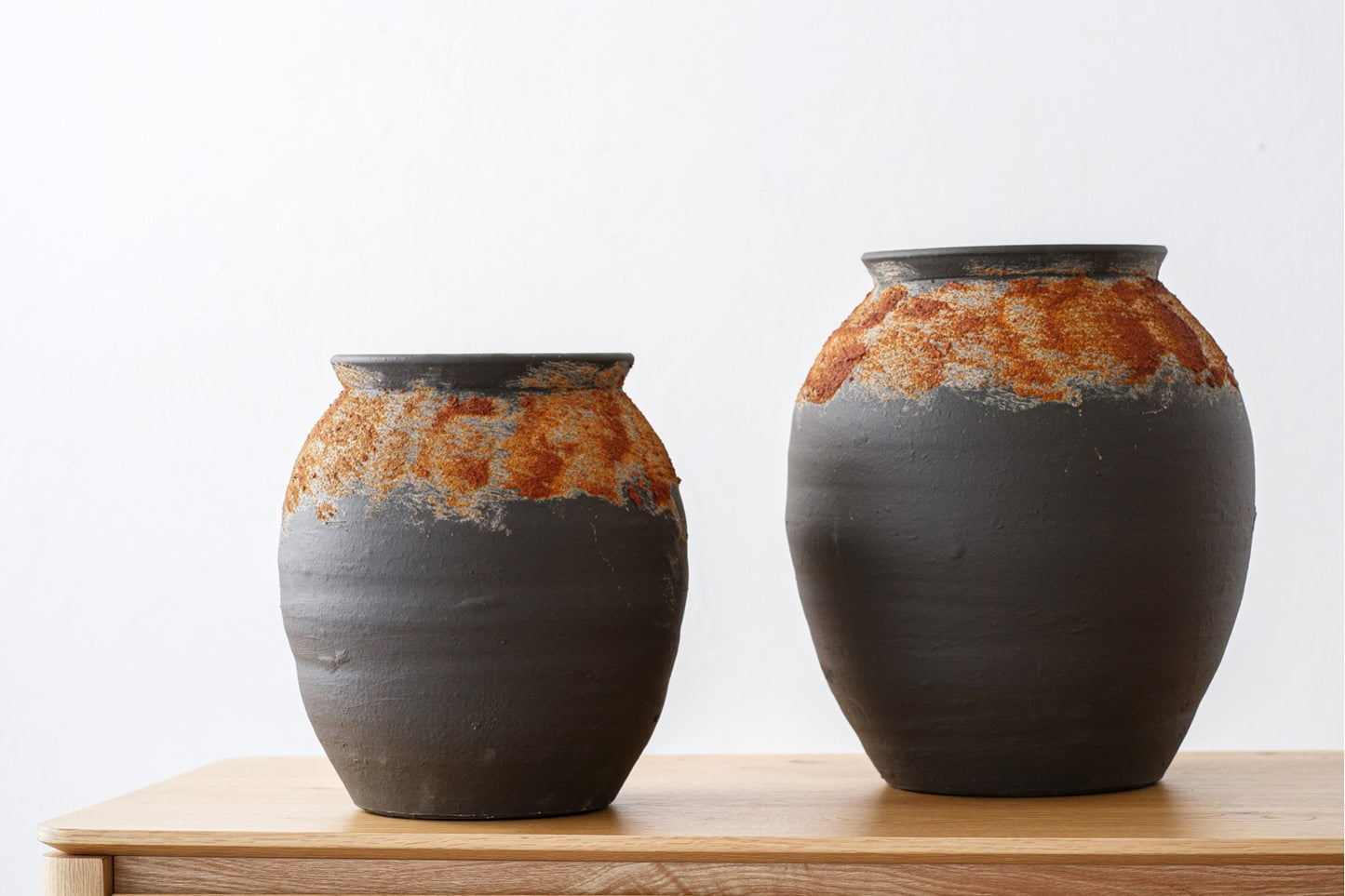 Set de vasijas de cerámica negro óxido pequeña y grande FERRO, estilo rústico, con bases oscuras y bandas texturizadas en tono óxido cerca del borde, sobre madera clara y fondo blanco.