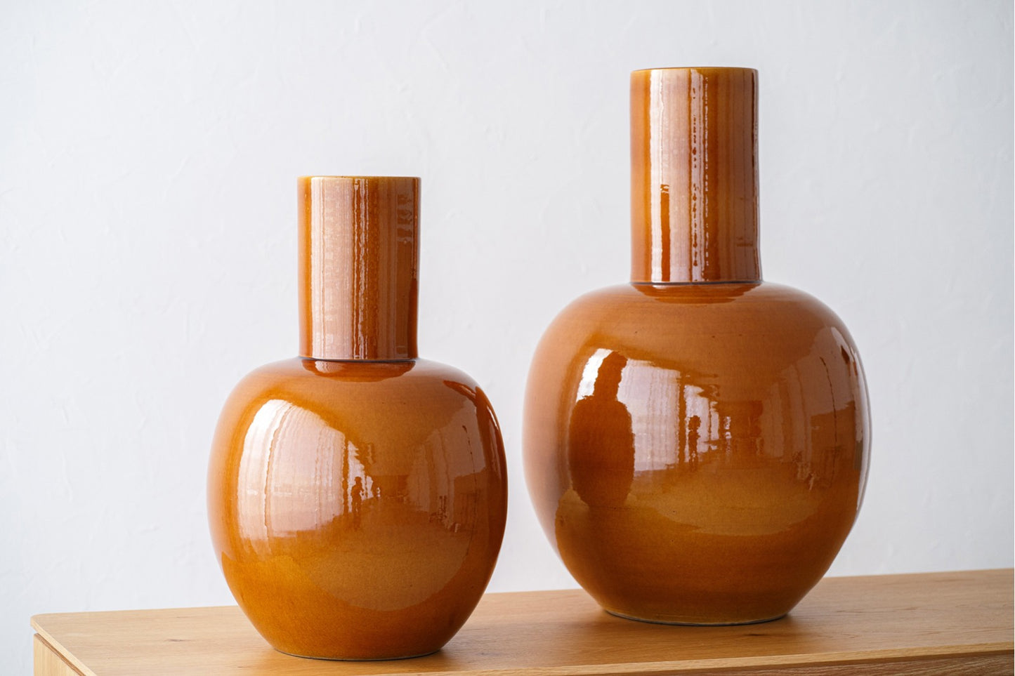 El set de jarrones de cerámica NELA, en amarillo dorado y dos tamaños, destaca sobre madera y fondo blanco; elegantes e ideales para dar un toque artesanal a la decoración del hogar.