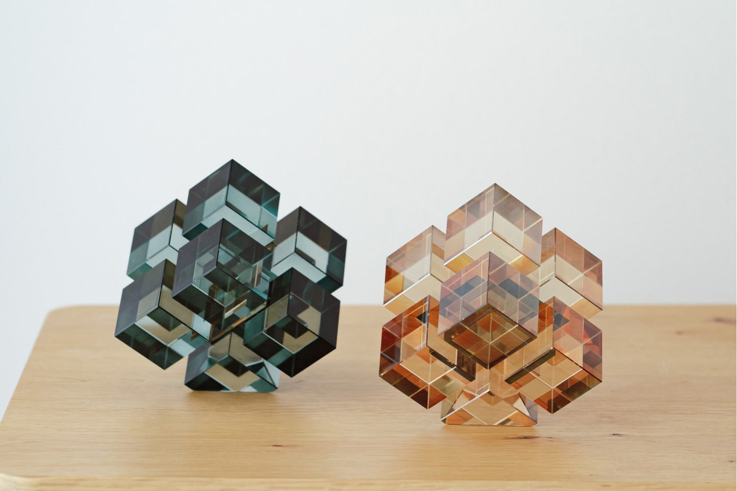 Dos piezas decorativas geométricas en cristal turquesa y champán, del set PUZZLE, se exhiben juntas sobre madera clara, destacando como elegantes elementos frente a un fondo blanco.