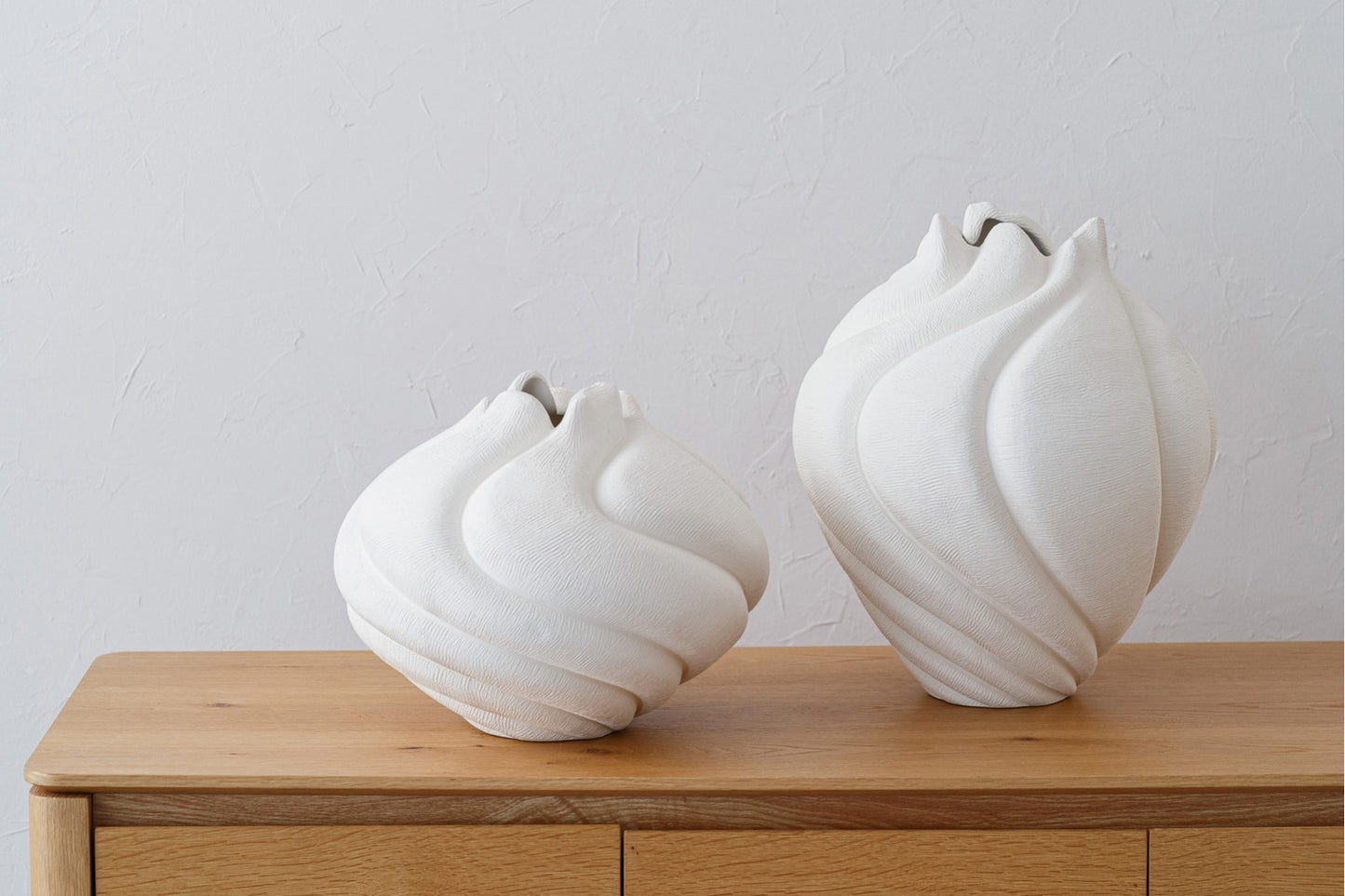 El set de jarrón y centro de cerámica blanco mate - orgánicos - RISCO destaca sobre un mueble de madera clara y pared texturizada, creando un elegante punto focal ideal para una decoración minimalista.