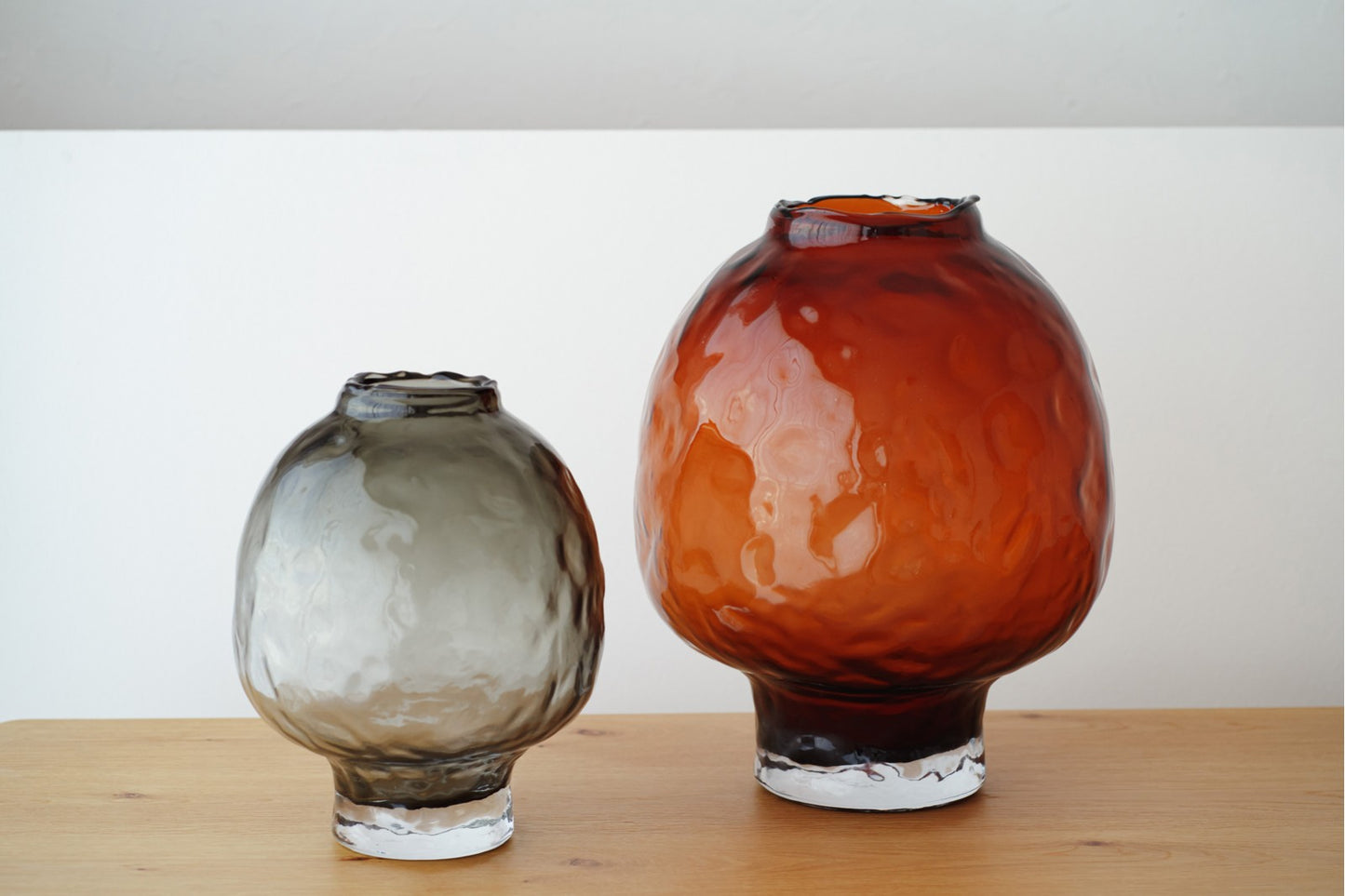 El set de jarrones de vidrio ámbar y gris redondeados SALETA decora perfectamente tu hogar, destacando sobre una superficie de madera y un fondo blanco.