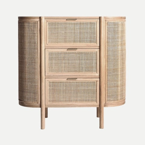 La cómoda en madera de mango y ratán IKLA, de diseño minimalista, tiene tres paneles frontales tejidos, lados curvos y cuatro patas; destaca sobre un fondo neutro.