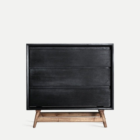 La cómoda moderna en madera mindi Thiers, de color negro con base de madera natural y tres cajones, es perfecta para un dormitorio actual y resalta sobre un fondo claro y sencillo.