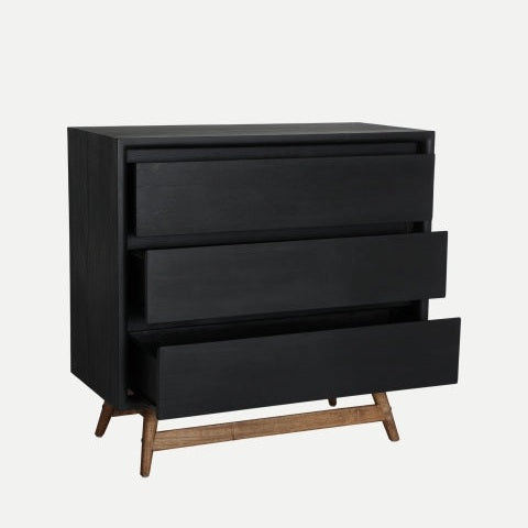Una Cómoda moderna en madera mindi Thiers negra con tres cajones parcialmente abiertos sobre patas de madera en ángulo se alza sobre un fondo liso, ideal para un dormitorio moderno que busca estilo y funcionalidad en almacenamiento.