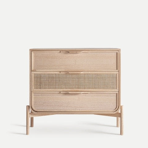 La cómoda en madera de fresno con ratán Weurtz tiene tres cajones, el central con frente de tejido de ratán, y ofrece almacenamiento ideal y diseño elegante sobre fondo claro.